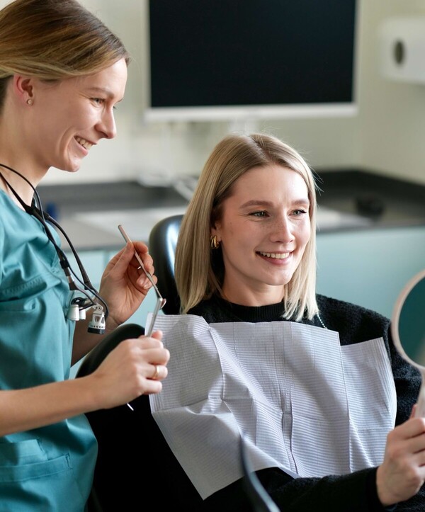 Isabell Jordan und eine Patientin betrachten gemeinsam das Ergebnis der Behandlung in einem Handspiegel, den die Patientin hebt.