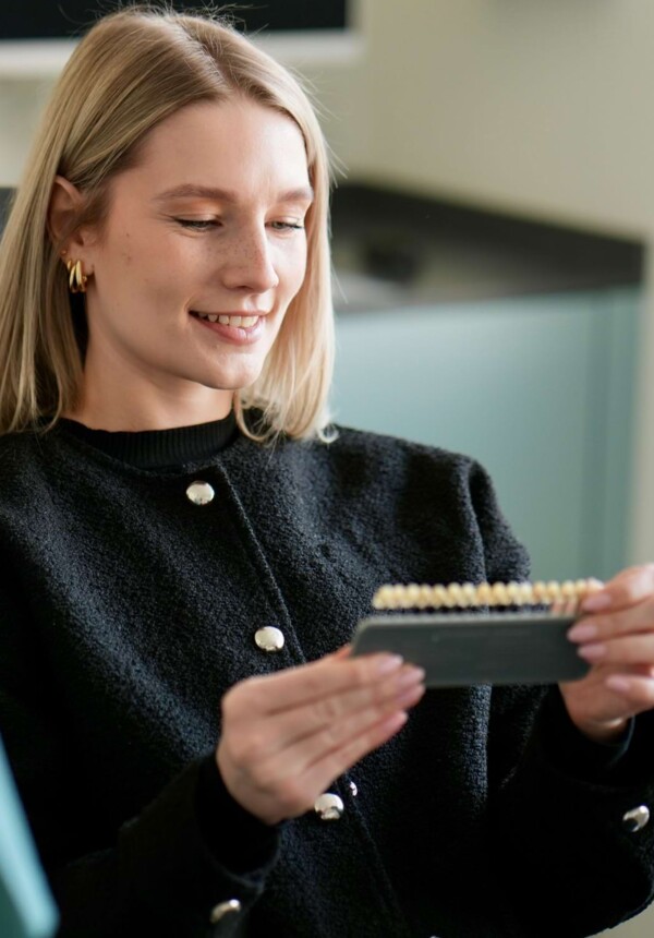 Eine Patientin h&auml;lt eine Zahnfarbskala und betrachtet die Skala.