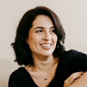 Portr&auml;t einer l&auml;chelnden Frau mit dunklem, schulterlangem Haar und einer feinen Halskette.