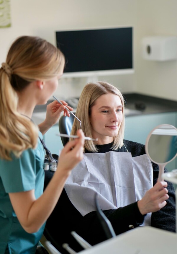 Foto einer Behandlungssituation. Isabell Jordan h&auml;lt Instrumente und die Patientin betrachtet sich in einem Handspiegel.